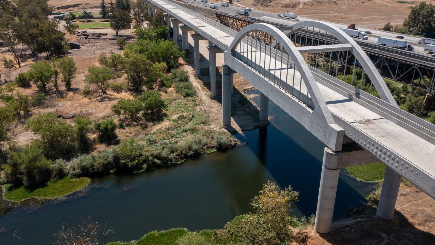 A concrete railway viaduct crosses a river, with its arch and surrounding landscape visible.